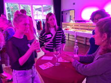 4 Frauen stehen um einen Tisch mit Gläsern und sprechen