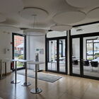 Raum mit 4 Stehtischen, runden Lampen, Blick auf umrahmte Glastür, dahinter Seminarraum mit Stühlen