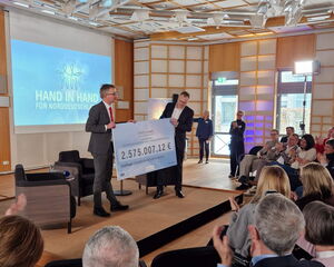 2 Männer mit einem großen Scheck vor Publikum, im Hintergrund eine Leinwadn "Hand in Hand für Norddeutschland"