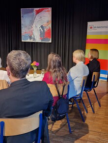Gäste an kleinen Tischen mit Blumen und Getränken, im Hintergrund ein Roll-up vom Paritätischen Bremen