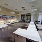 Heller Seminarraum mit weißen Tischen im Carree gestellt, links Bilder an der Wand, rechts Säule und Fenster