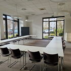 Heller Seminarraum mit weißen Tischen und ca. 15 Stühlen in Hufeisenform gestellt, Fenster zum Parkplatz, Bild an der Wand