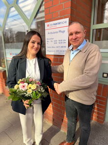Eine junge Frau mit Blumenstrauß neben einem Mann, im Hintergrund ein Schild des Paritätischen BHV, Ambulante Pflege