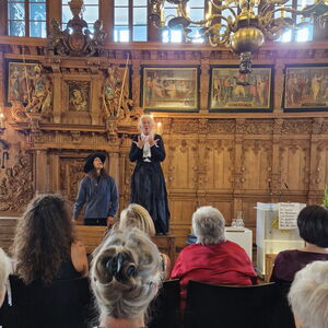Personen im Bremer Rathaus blicken auf eine Darstellerin in schwarzem Kleid, die eine historische Figur darstellt