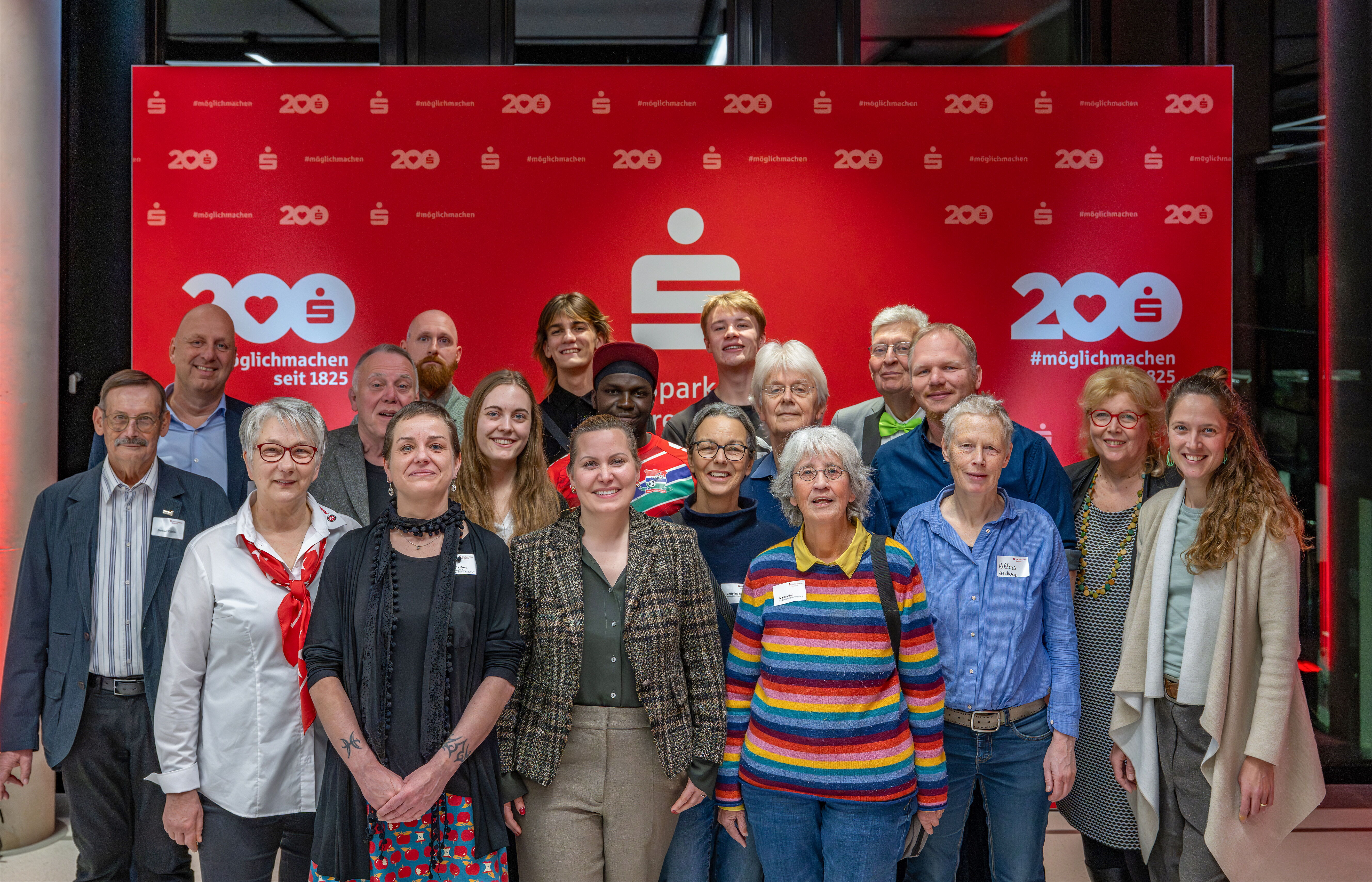 Gruppe von freudigen Menschen vor einer roten Wand der Sparkasse