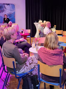 Gäste sitzen an kleinen Tischen mit Blumen und Getränekn