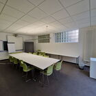 Seminarraum mit großem Tisch, grünen Stühlen, im Hintergrund, Whiteboard, Flipchart, Fenster Glasbausteine