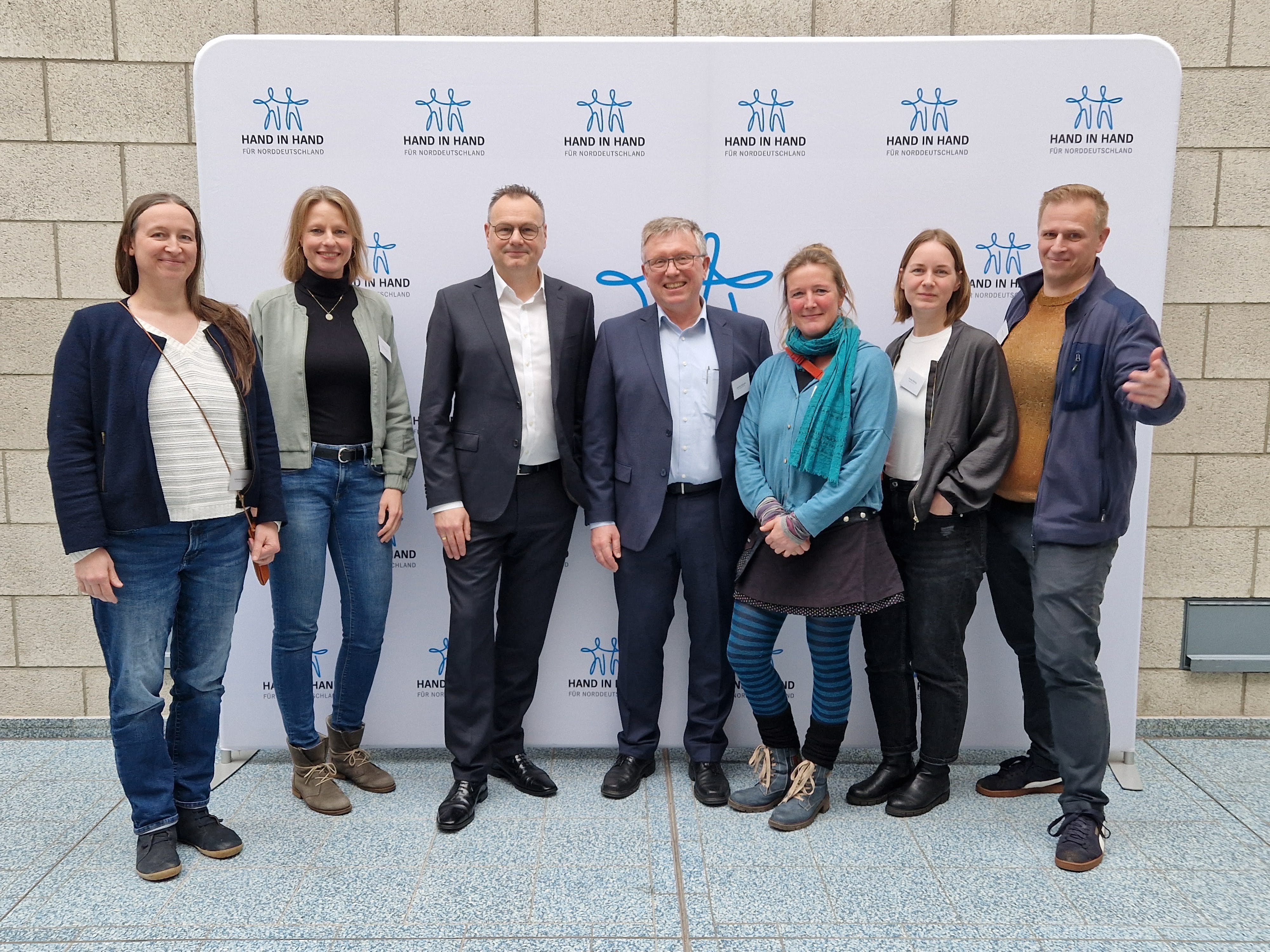 7 Personen vor einer Logowand Hand in Hand für Norddeutschland